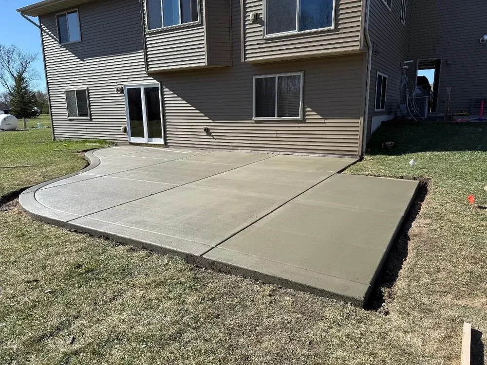 New broom-finished patio with curved border behind a split-level home
