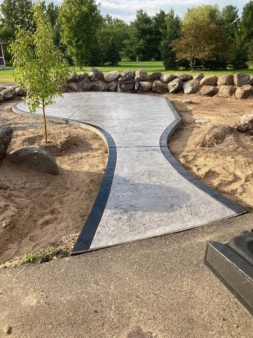 Stamped concrete walkway with charcoal border winding past a boulder retaining wall