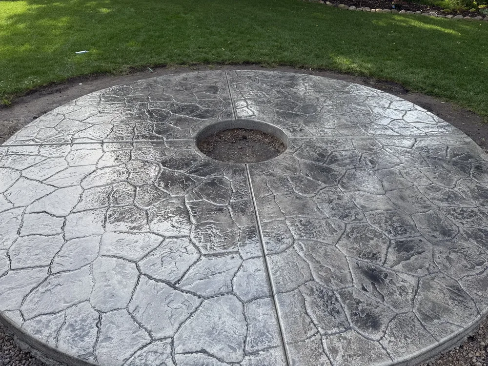 Circular stamped concrete fire pit surround in a flagstone pattern set into a lawn