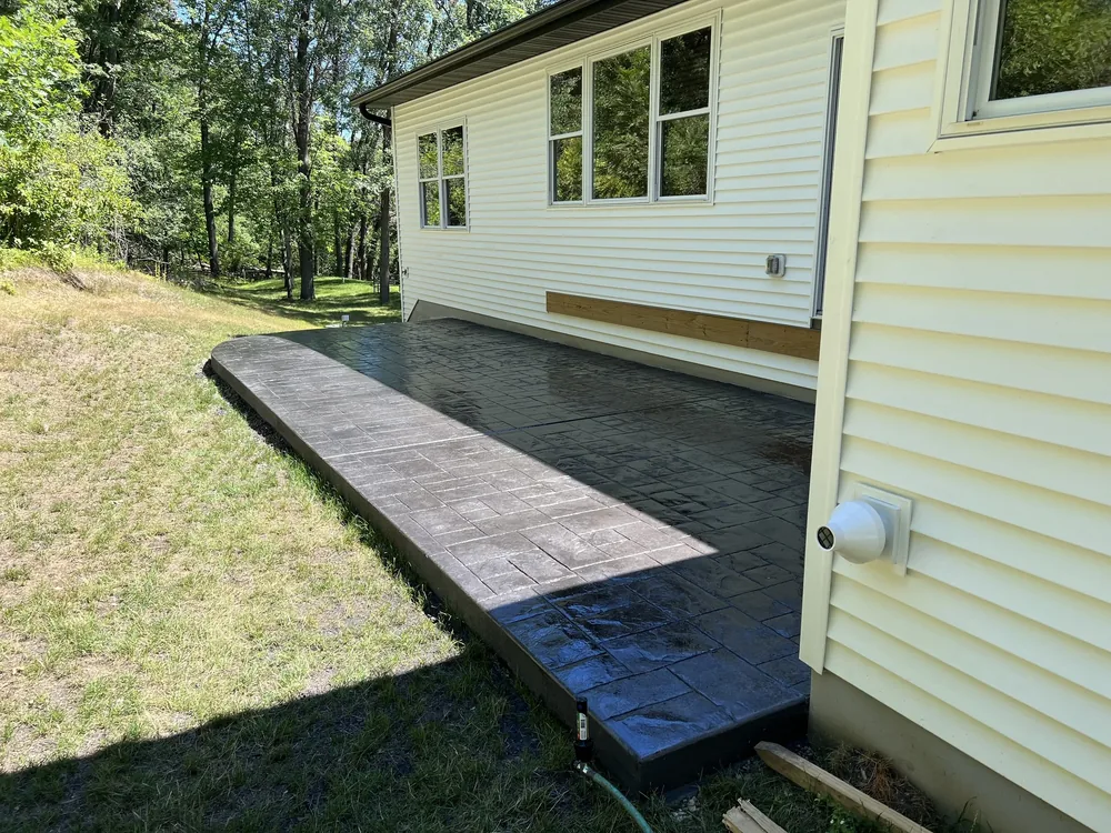 Dark stamped concrete patio in a cobblestone pattern along a white house