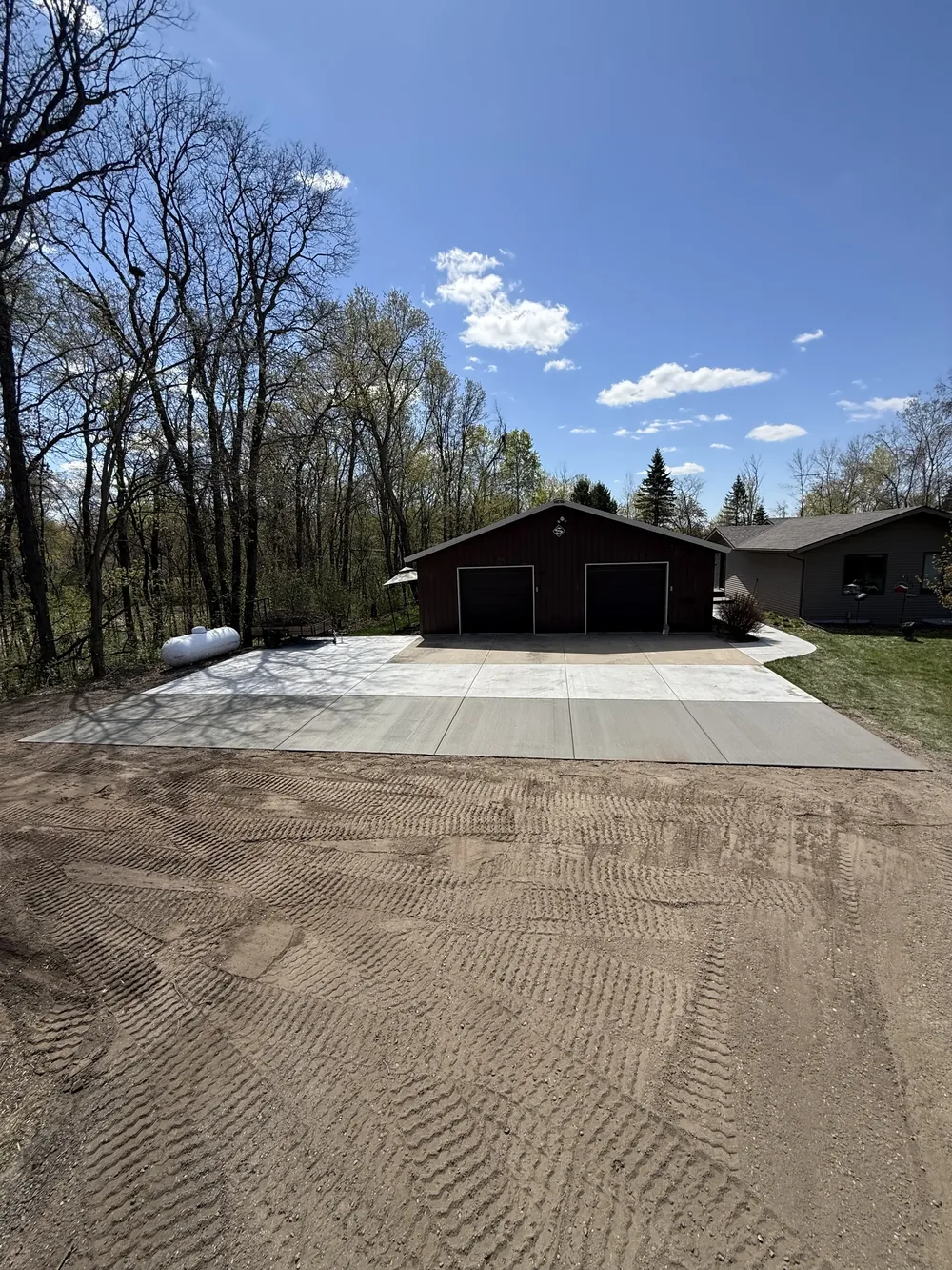 Wide concrete garage apron and driveway pad in front of a dark pole barn garage