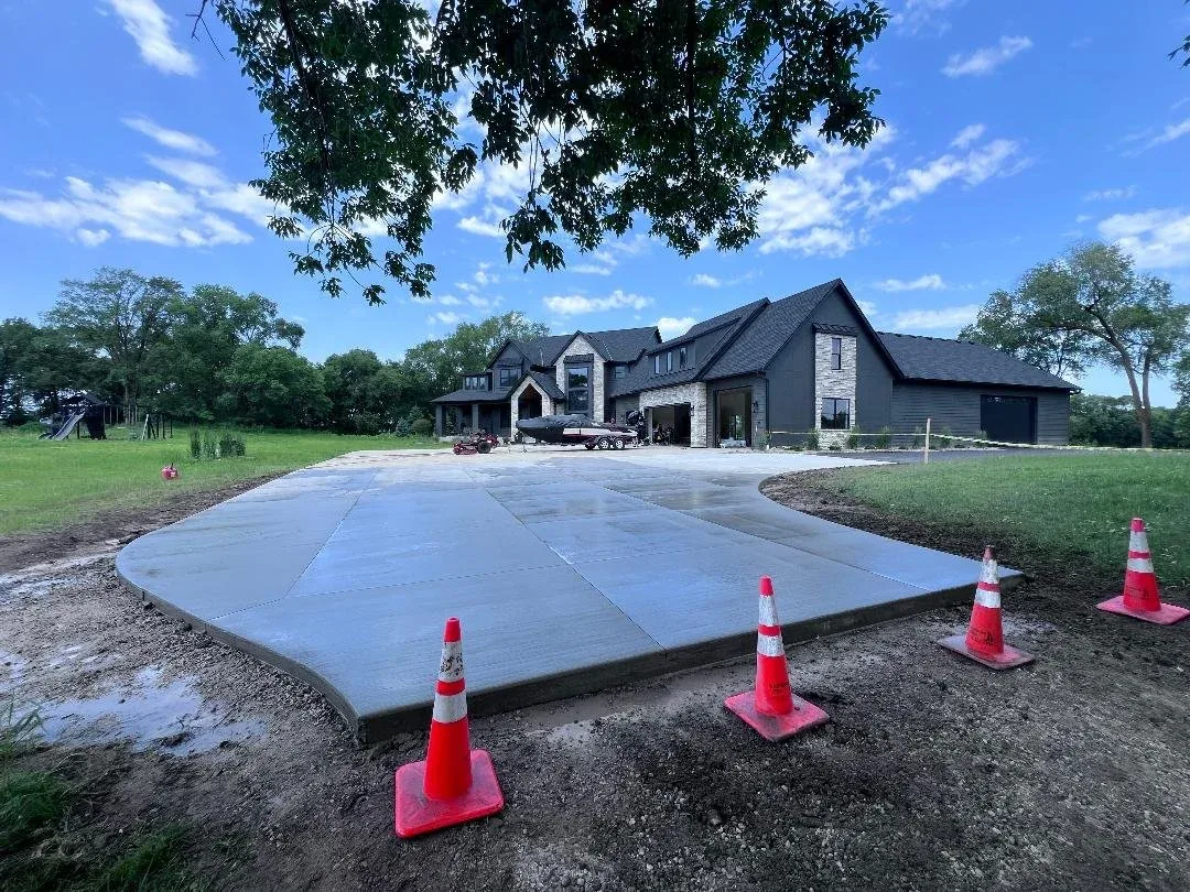 New concrete driveway curving toward a large two-story home with a boat parked by the garage