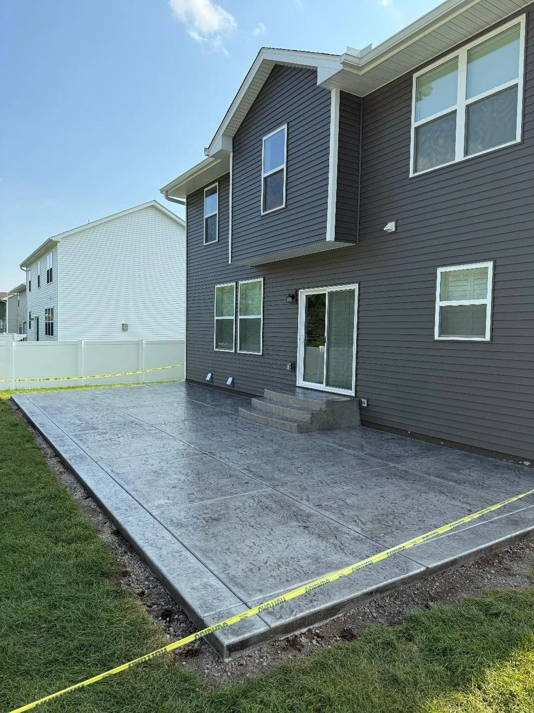 Large stamped concrete patio in a slate pattern with curved steps behind a gray two-story house